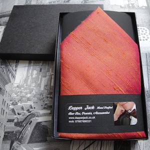 May include: A red and orange silk pocket square in a black box. The box has a label that says "Dapper Jack Hand Crafted Bow Ties, Cravats, Accessories www.dapperjack.co.uk mob: 07887898331"