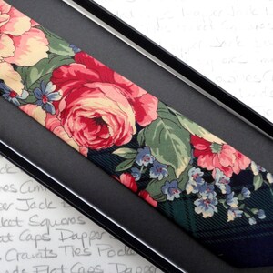 May include: A dark green and black patterned tie with a floral design featuring pink, red, and white roses and blue flowers.