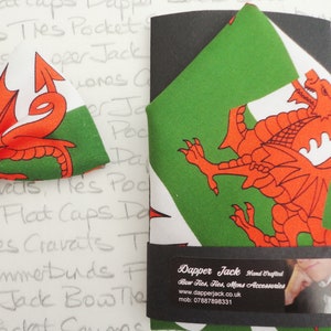 May include: A red dragon on a white and green background bow tie and pocket square. The fabric features the Welsh flag. The pocket square is folded and packaged with a black label that reads "Dapper Jack Hand Crafted Bow Ties, Ties, Mens Accessories www.dapperjack.co.uk mob: 07887898331"