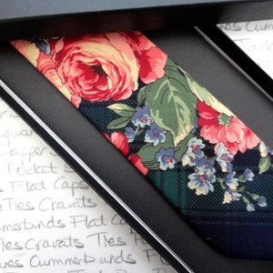 May include: A dark green and navy blue tie with a floral pattern featuring pink, yellow, and blue flowers. The tie is in a gift box.