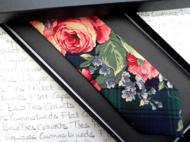 May include: A dark green and navy blue tie with a floral pattern featuring pink, yellow, and blue flowers. The tie is in a gift box.