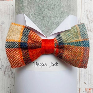 Op de afbeelding: Een geruite strik met oranje, beige, blauwe en groene kleuren. De strik is geknoopt en wordt getoond op een wit oppervlak met de tekst "Dapper Jack" erop gedrukt.