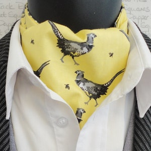 Puede incluir: Una corbata amarilla con un patrón repetido de faisanes negros y blancos. La corbata está atada alrededor de un cuello de camisa blanco y una chaqueta negra.