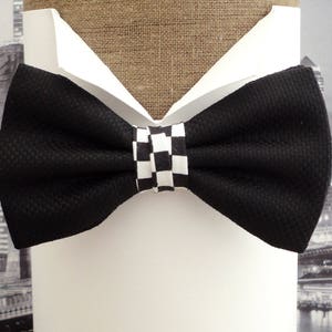 May include: A black bow tie with a white and black checkered pattern in the center. The bow tie is displayed on a white shirt.