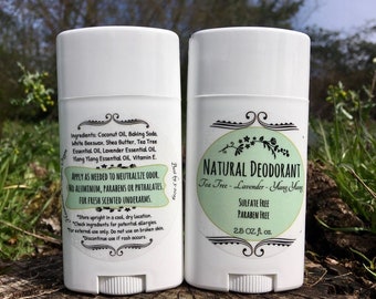 May include: Two white deodorant sticks with green and black labels. The label on the left stick lists ingredients and instructions for use. The label on the right stick reads "Natural Deodorant", "Tea Tree - Lavender - Ylang Ylang", "Sulfate Free", "Paraben Free", and "2.5 OZ. fl. oz."