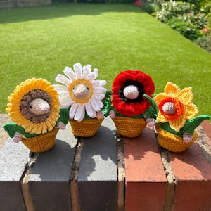 May include: Four crocheted flower pot characters, each with a different flower and a small mouse face. The flowers are a sunflower, a daisy, a poppy, and a daffodil. The characters are sitting on a brick wall.