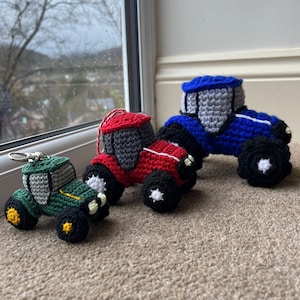 May include: Three crocheted toy tractors in different sizes. The smallest is green, the middle is red, and the largest is blue.