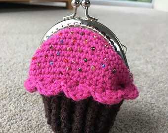 May include: A pink and brown crocheted cupcake coin purse with a silver clasp and colorful beads.