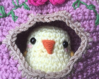 May include: A crocheted birdhouse with a pink flower on top and a yellow chick peeking out of the opening.
