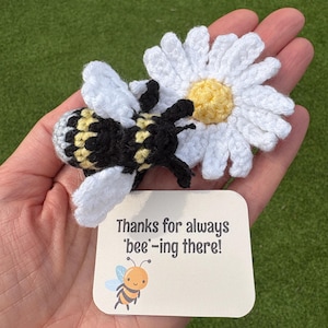 Könnte beinhalten: Gehäkelte Biene und Gänseblümchen mit einer Karte mit der Aufschrift "Thanks for always 'bee'-ing there!". Die Biene ist schwarz, gelb und grau, mit weißen Flügeln. Das Gänseblümchen hat weiße Blütenblätter und eine gelbe Mitte. Die Karte hat eine Cartoon-Biene.