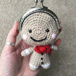 May include: A crocheted gingerbread man coin purse with a red bow, black eyes, and pink cheeks. The purse has a silver metal clasp.