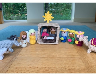 May include: A crocheted nativity scene featuring figures of Mary, Joseph, baby Jesus, angels, wise men, a donkey, a sheep, and a camel. The figures are in various colors, including beige, blue, yellow, and pink. A yellow star sits atop the stable.