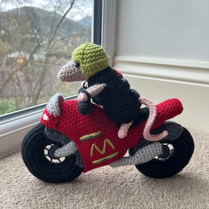 Peut inclure: Une souris en crochet portant un casque vert et une veste noire, conduisant une moto en crochet rouge et noire.