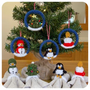 May include: Crocheted Christmas decorations including a snowman, penguin, Christmas tree, and candle. Each is suspended within a blue crocheted ring. The decorations are displayed on a Christmas tree and on a table.