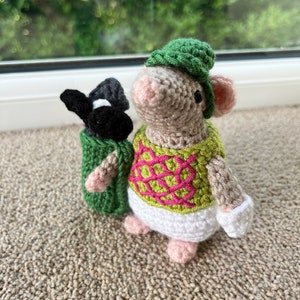 Może przedstawiać: Szydełkowana mysz w zielonym kapeluszu i różowo-zielonej kamizelce, trzymająca czarną i białą torbę golfową.