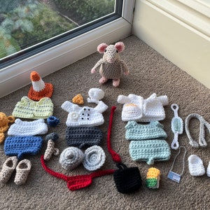 Op de afbeelding: Een verzameling gehaakte outfits en accessoires voor een klein knuffeldier. De outfits omvatten een koksuniform, een doktersjas, een bouwvakkersvest en een badpak. De accessoires omvatten een hoed, een stethoscoop, een gereedschapsgordel en een tas.