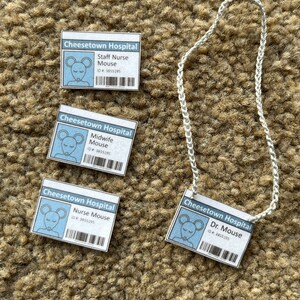 Op de afbeelding: Vier witte ID-badges met blauwe accenten en cartoonmuizen. De badges zijn voor een verpleegkundige, een verloskundige, een verpleegkundige en Dr. Mouse. De badges zijn allemaal van het Cheesetown Hospital en hebben het ID-nummer 3855195. De badges hangen aan een wit touwtje.
