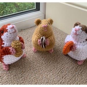 May include: Three crocheted hamster plushies holding different colored crocheted treats. The hamsters are brown, orange, and white with pink noses and feet.