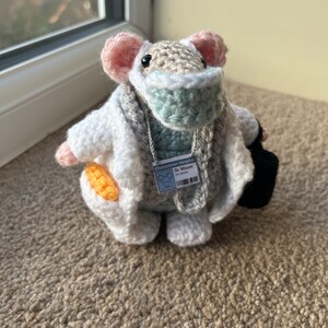 Op de afbeelding: Een gehaakte muis die een witte doktersjas, een blauw mondkapje en een naamplaatje draagt met de tekst "Cheshire Hospital Dr. Mouse".