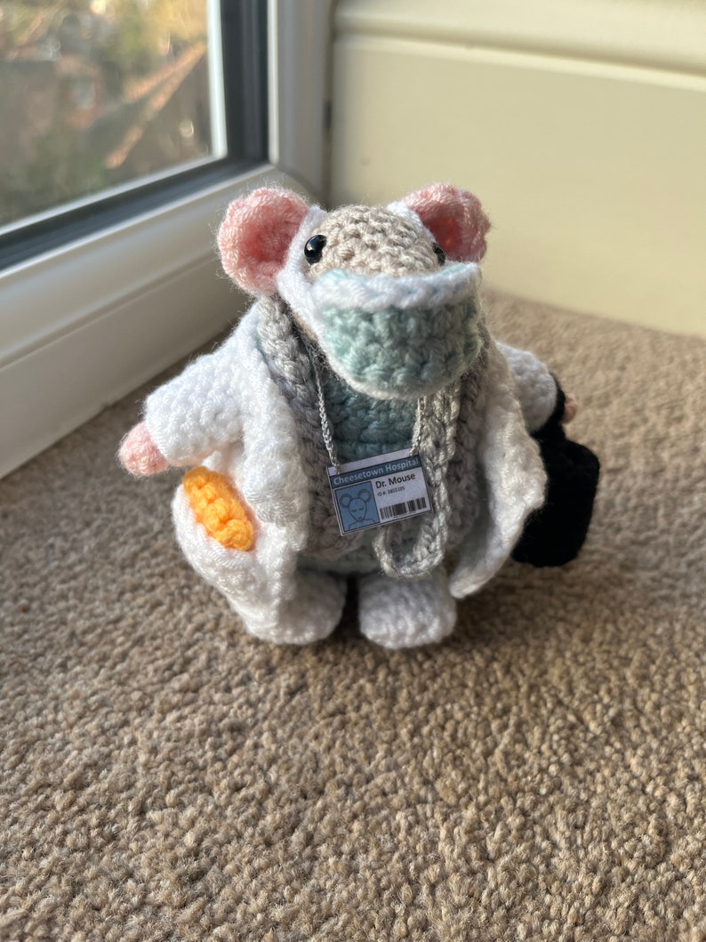 Op de afbeelding: Een gehaakte muis die een witte doktersjas, een blauw mondkapje en een naamplaatje draagt met de tekst "Cheshire Hospital Dr. Mouse".