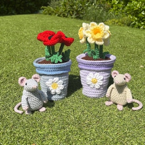 May include: Two crochet flower pots with red poppies and yellow daffodils, and two crochet mice, all set on green grass. The flower pots are blue and purple with white daisy accents. The mice are gray and beige.