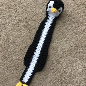Puede incluir: Un marcapáginas de pingüino de crochet negro y blanco con patas amarillas y un pico amarillo.