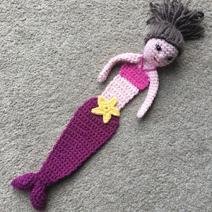 May include: A crocheted mermaid doll with pink and purple yarn, a yellow star on her tail, and brown yarn hair.