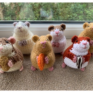 May include: Six crocheted hamster plushies in various colors, each holding a different food item. The hamsters are sitting on a brown carpet.