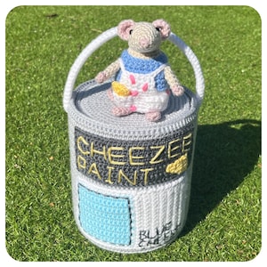 May include: A crocheted gray paint can with a white lid and a blue paint swatch. The can has the words "Cheeze Paint" on the front. A crocheted white mouse with pink ears and a blue and white vest is sitting on the lid.