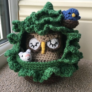 Puede incluir: Un búho de crochet con los ojos cerrados, un pequeño ratón de crochet y un pájaro azul sentado en un nido de crochet verde.