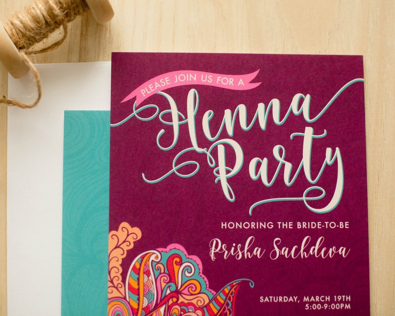 May include: A burgundy invitation with a pink banner that says "Please join us for a Henna Party". The invitation is decorated with a colorful paisley design and the text "Honoring the bride-to-be Prisha Sachdeva" and "Saturday, March 19th 5:00-9:00PM".