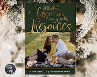 May include: A Christmas card with a green background and gold lettering that reads "A thrill of hope the weary world rejoices". The card features a photo of a couple sitting on a blanket in a field. The text "Merry Christmas | The Kristman Family" is at the bottom of the card.