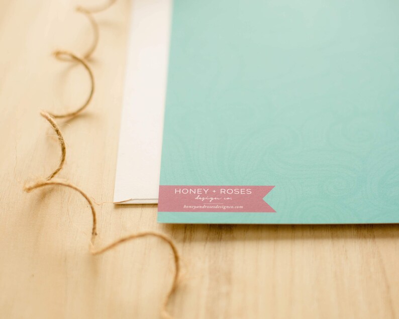May include: A light blue card with a pink banner that says "Honey + Roses" and a website address. The card is on a wooden surface.