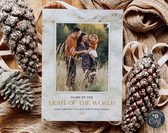 May include: A Christmas card with a marble background and gold accents. The card features a photo of a family of three in a field. The text on the card reads "Glory to the Light of the World" and "Merry Christmas Love, Jack, Stella & Charlie Goodison 2023".