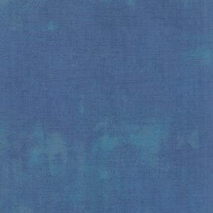 May include: A close-up of a blue fabric with a textured appearance. The fabric has a mottled effect with lighter blue and teal accents, creating a watercolor-like aesthetic. The material appears to be a woven textile.