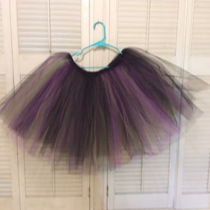 May include: A black, purple, and green tulle tutu skirt hanging on a blue hanger. The skirt is layered and fluffy.