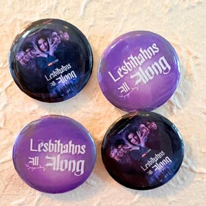 May include: Four purple and black round buttons with the text "Lesbians All Along" in white lettering. The buttons feature a black and white image of a group of people.