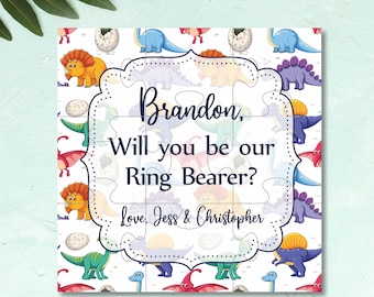 May include: A white puzzle piece with a dinosaur pattern. The puzzle piece has a message that says "Brandon, Will you be our Ring Bearer? Love, Jess & Christopher".