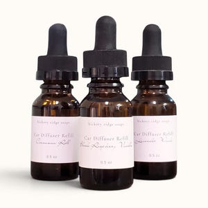 May include: Three brown glass bottles with black droppers, labeled "Car Diffuser Refill." The labels read "Cinnamon Roll," "Black Raspberry Vanilla," and "Lavender Woods." Each bottle contains 0.5 oz of liquid.