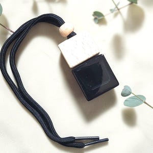 May include: A black and white car air freshener with a black cord. The air freshener has two square blocks, one black and glossy, the other white with a wood grain pattern. A small wooden bead is at the top.
