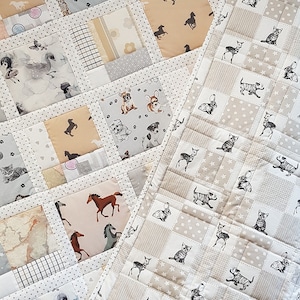 Puede incluir: Una colcha de retazos con una variedad de estampados de animales, incluyendo caballos, gatos, perros y ciervos. La colcha está hecha de telas beige, gris y blanco. La colcha está hecha en estilo patchwork con cuadrados de diferentes telas cosidos juntos. La colcha está bordeada con un borde blanco.
