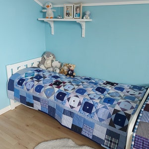 Puede incluir: Una cama blanca con una colcha de patchwork azul y blanco. La cama está en una habitación con paredes de color azul claro y una estantería blanca con animales de peluche y fotos enmarcadas.