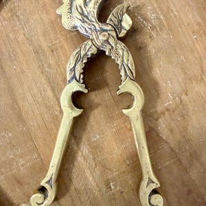 May include: A vintage brass nutcracker with a bird-like design. The nutcracker features a detailed head and leaf-like accents. The handles curve into a decorative shape. The brass has a warm, golden hue.