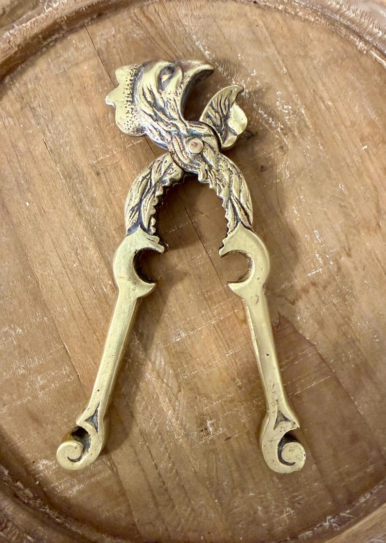 May include: A vintage brass nutcracker with a bird-like design. The nutcracker features a detailed head and leaf-like accents. The handles curve into a decorative shape. The brass has a warm, golden hue.
