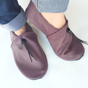 May include: A pair of mauve leather slippers with black drawstrings and a black button accent. The slippers have a soft, comfortable look.
