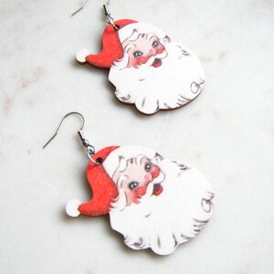 May include: A pair of festive earrings depicting Santa Claus. Each earring showcases Santa's face, complete with a red hat, white beard, and rosy complexion. The earrings are finished with silver-coloured ear wires.