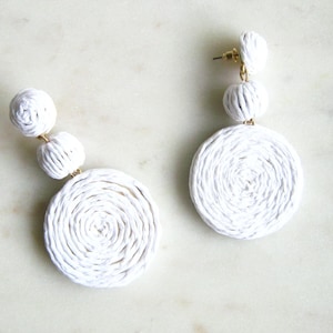 May include: White woven circle earrings with three smaller white woven balls hanging from the bottom.