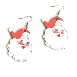 May include: A pair of Santa Claus earrings. Each earring depicts a smiling Santa face with a red hat, rosy cheeks, and a white beard. The earrings are made of a lightweight material and have silver-coloured fish hook ear wires.