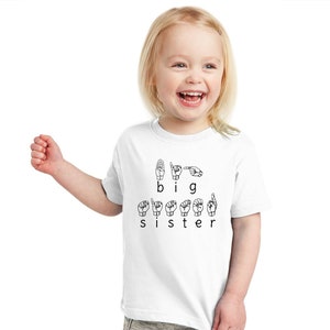 May include: A white t-shirt with the words "I am a big sister" spelled out in British Sign Language.