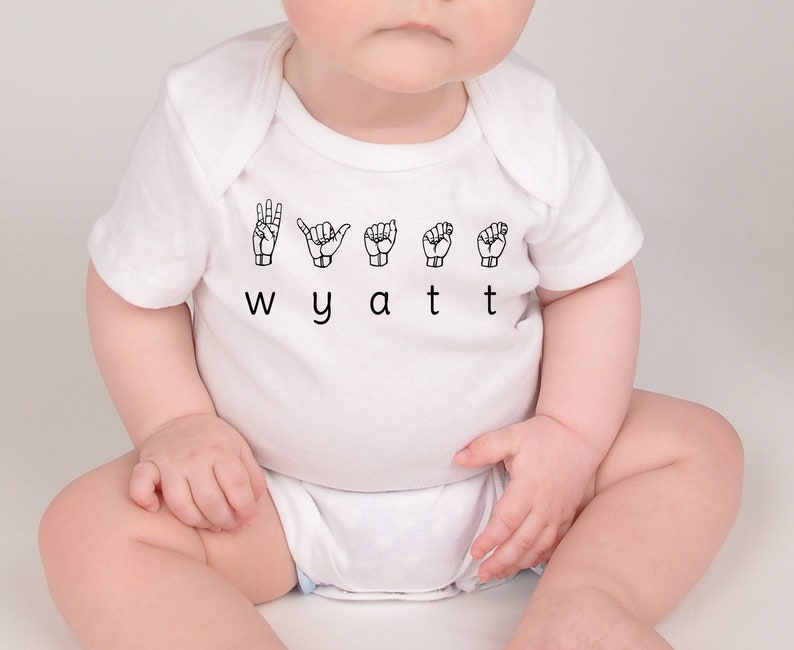 May include: White baby onesie with the name "Wyatt" spelled out in black letters and the letters signed in British Sign Language.